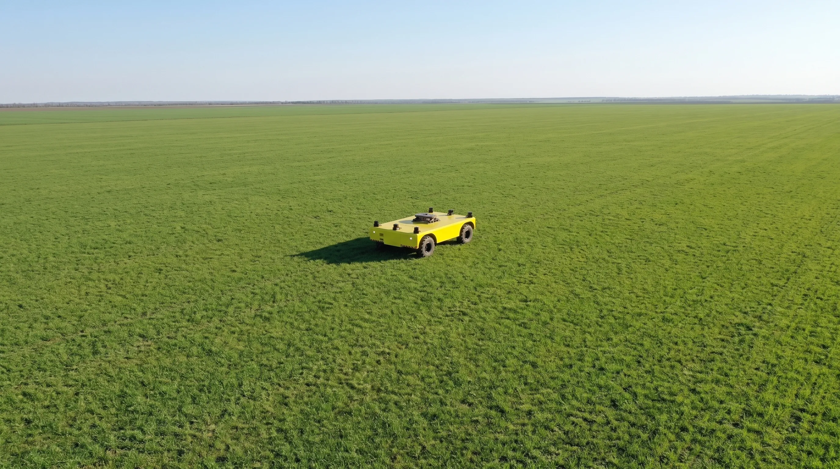 Aerial view of a single yellow autonomous platform transporter alone in the middle of a large green field.